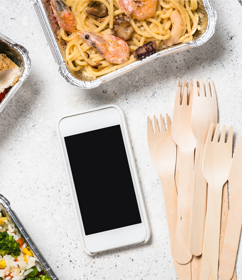 A phone, disposable utensils, and delivered food on a table