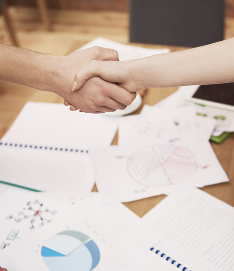 A handshake over a table filled with business-related papers